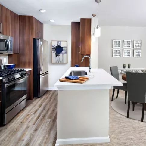A contemporary kitchen with stainless steel appliances, wood cabinetry, and a quartz countertop island, leading into a stylish dining area.