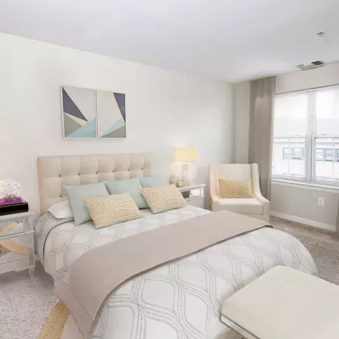 A bright and spacious bedroom with a plush, tufted headboard, elegant neutral-toned bedding, and modern décor at The Mark at Mamaroneck Luxury Apartments.