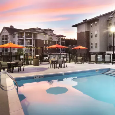 A stunning sunset over the pool area, reflecting soft colors in the water, with orange umbrellas and lounge chairs for relaxation.