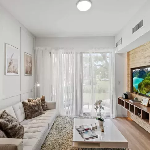 The Oak Enclave apartments offer a modern living space with a mounted TV, floor-to-ceiling windows, and an inviting atmosphere.