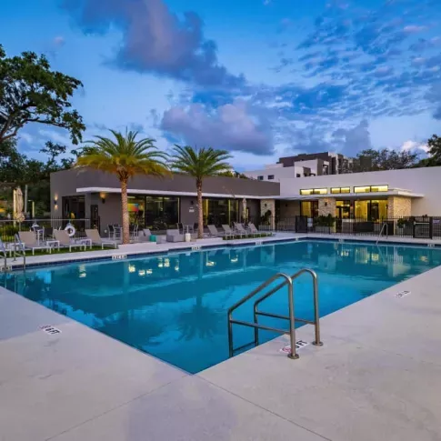 The pool at Oak Enclave illuminated at dusk, showcasing a peaceful and inviting atmosphere with warm lighting and stylish seating.