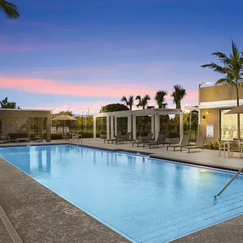 A resort-style pool at sunset with poolside seating, cabanas, and lush palm trees, creating a tranquil retreat for residents.