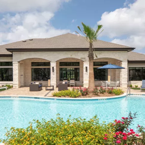 Clubhouse exterior at Vista At Town Green, featuring elegant stone architecture, large windows, and a beautifully landscaped pool area for residents to enjoy.