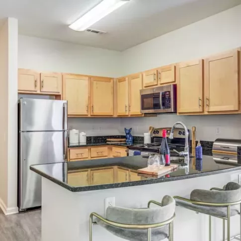 A stylish kitchen in an Oak Enclave apartment, showcasing stainless steel appliances, wooden cabinetry, and a sleek black granite countertop with bar seating.