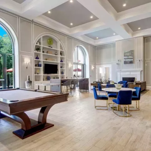 A stylish clubroom with high ceilings, a pool table, and comfortable seating, featuring large windows and access to outdoor spaces.