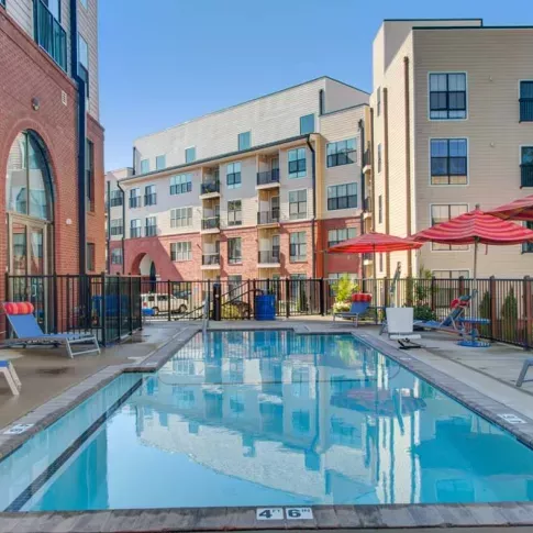 A closer view of the resort-style pool at The Royal Belmont, with red umbrellas, comfortable seating, and arched building entrances.