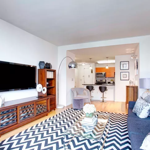 A modern living room with large windows offering city views, stylish furniture, and a bold zigzag patterned rug, creating a vibrant and cozy ambiance.