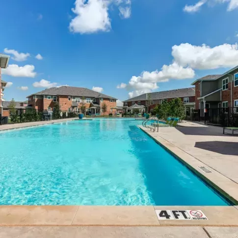 Expansive pool area with crystal-clear water and poolside seating at The Emerson at Forney Luxury Apartments, perfect for relaxation.