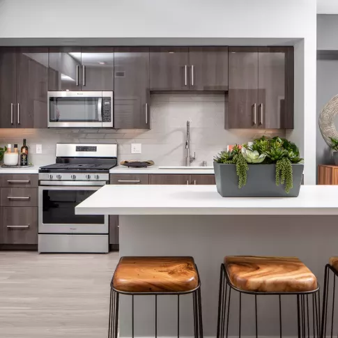 "Modern kitchen at The Pacific Luxury Apartments featuring sleek dark cabinetry, stainless steel appliances, a stylish white island with natural wood bar stools, and elegant décor accents."