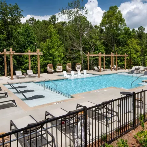 An inviting pool with lounge chairs, surrounded by lush trees and pergolas on a sunny day.