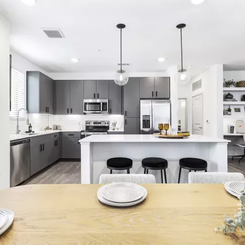 A stylish dining space with a wooden table set for a meal, seamlessly connected to a modern kitchen with pendant lighting and sleek finishes.