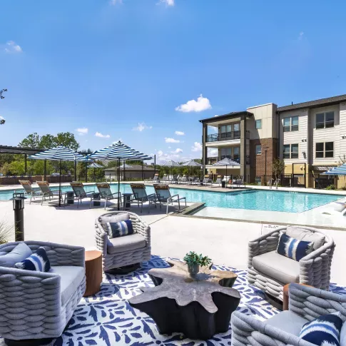 The luxury pool area features stylish woven chairs, a sculptural table, and blue-patterned umbrellas, offering a perfect spot for relaxation.