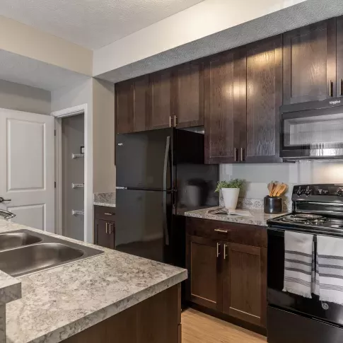 A modern kitchen with dark wood cabinetry, granite countertops, and a double sink at Victoria Manor Luxury Apartments.
