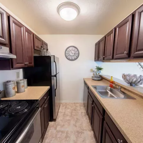 Well-equipped kitchen with sleek countertops, stainless steel appliances, and classic dark wood cabinetry at Forest Creek Apartments