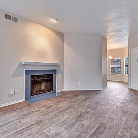 Spacious living area featuring wood-style flooring, a cozy fireplace with a white mantle, and a view into the dining nook near the front entrance.