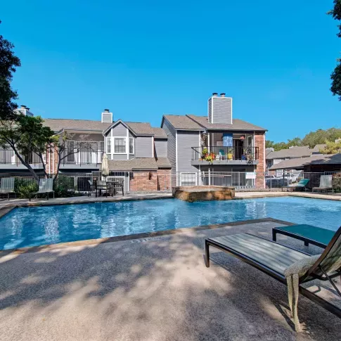 View of the community swimming pool with water feature, surrounded by lounge seating and multi-story residential buildings.