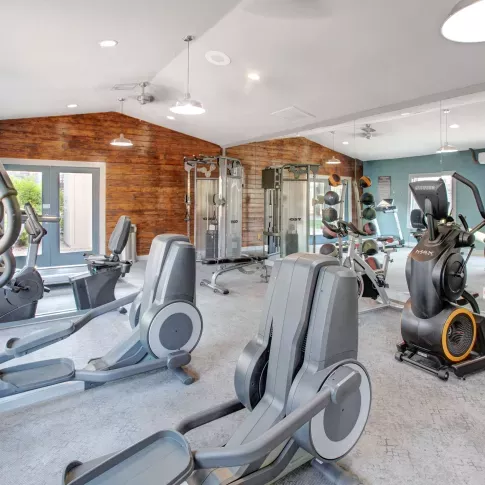 Fitness center with cardio and strength training equipment, including ellipticals, stationary bikes, and free weights, set against wood-accented and mirrored walls.
