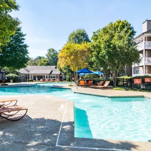 Resort-style swimming pool surrounded by orange lounge chairs and shaded seating under blue umbrellas.