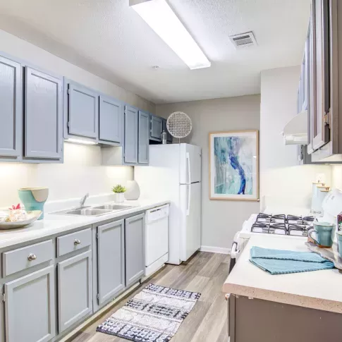 Galley-style kitchen with soft gray cabinets, white appliances, and wood-style flooring.