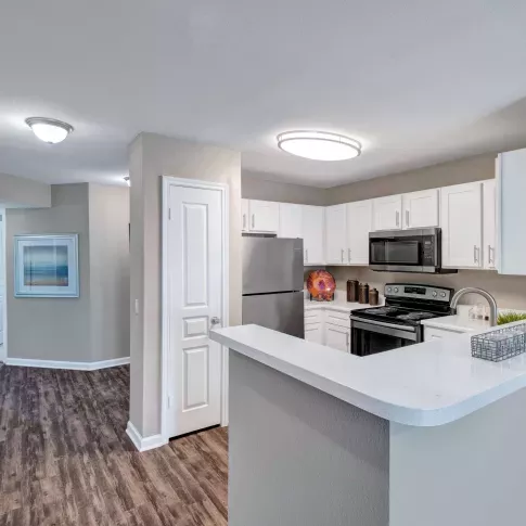 Modern kitchen with stainless steel appliances, white cabinets, and wood-style flooring.