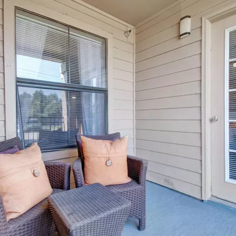 Private balcony with wicker chairs and a small table, adjacent to a large window and French door.