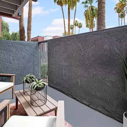 Private patio with stylish outdoor seating and potted plants, surrounded by tall palm trees and modern apartment exteriors.