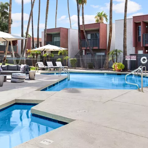 Pool area with lounge chairs, shaded seating, and palm trees at a modern apartment community.