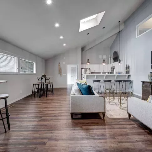 Modern resident clubhouse with vaulted ceilings, skylight, wood-style flooring, bar seating, and contemporary lounge furniture with a mounted TV and kitchen area.