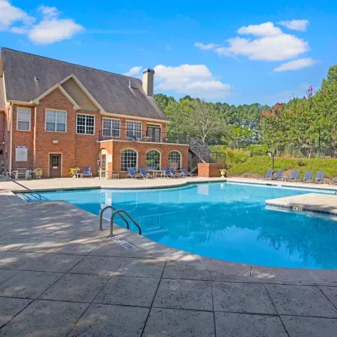 Inviting resort-style swimming pool surrounded by ample lounge seating and lush landscaping, set against the elegant brick exterior of the Holland Park clubhouse.