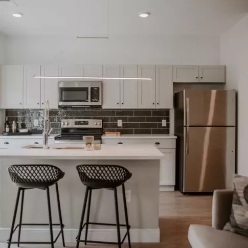 Open-concept kitchen with a spacious island, pendant lighting, and a mix of contemporary finishes, including a black tile backsplash and stainless steel appliances.