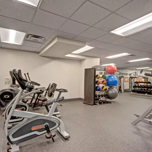Spacious fitness center featuring cardio machines, free weights, resistance equipment, and colorful exercise balls in a brightly lit room with mirrored walls.