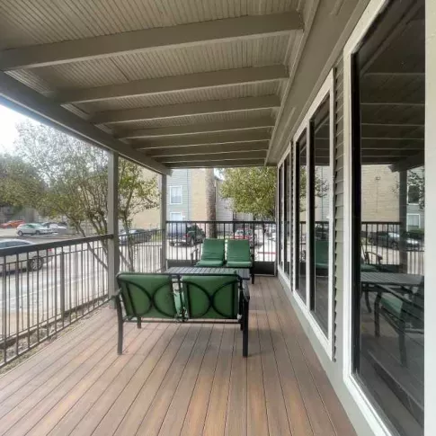 A covered outdoor lounge area with comfortable green seating at The Oaks of Westchase Apartments, perfect for relaxing while enjoying the view.