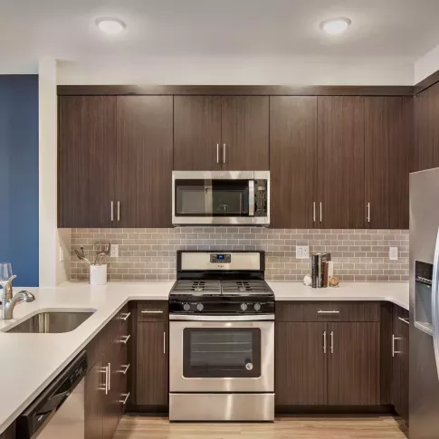 Modern kitchen featuring sleek dark wood cabinetry, stainless steel appliances including a gas range and microwave, and a built-in wine rack. The kitchen boasts a neutral subway tile backsplash and light quartz countertops, with an open layout and breakfast bar overlooking a cozy dining area. Perfect blend of contemporary style and functionality.