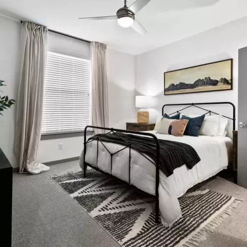A serene bedroom with a modern metal bed frame, cozy bedding, and a large window for natural light.