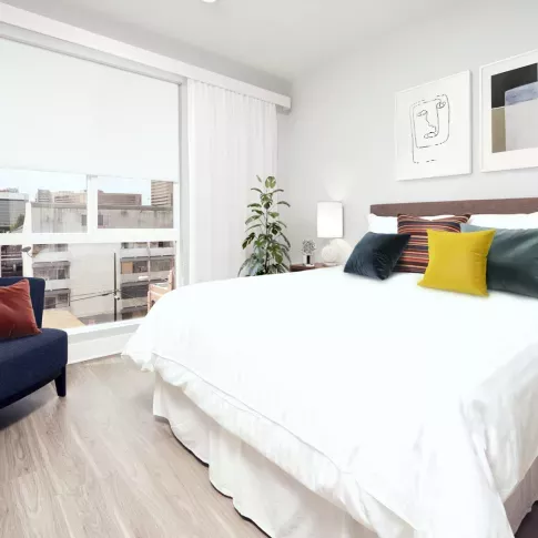 Bright bedroom with large window, modern decor, and wood-style flooring. 
