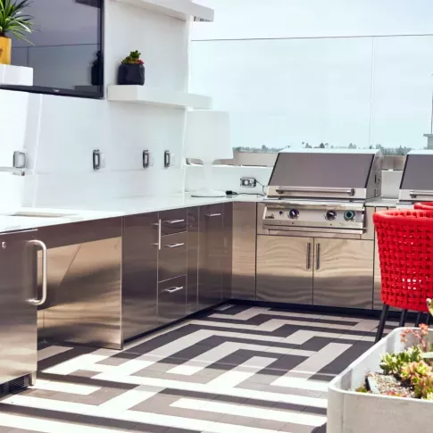 Outdoor rooftop kitchen area with stainless steel appliances, red barstools, and modern tile flooring.