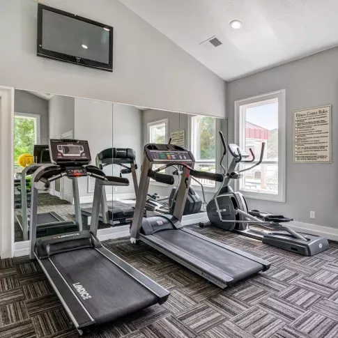Fully equipped fitness center at The Samuel with treadmills, elliptical machine, wall-mounted TV, and large windows providing natural light