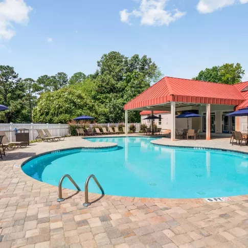 Outdoor swimming pool at The Samuel with lounge chairs, shaded tables, and a red-roofed pavilion surrounded by lush greenery