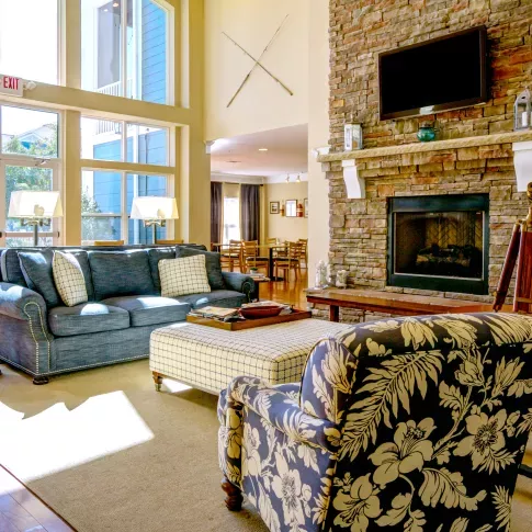 Bright community lounge with cozy furniture, a stone fireplace, and natural light from floor-to-ceiling windows