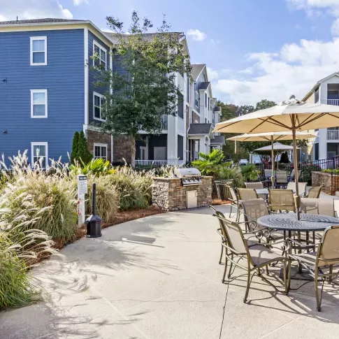 Grill and patio area with umbrella-shaded tables and lush landscaping