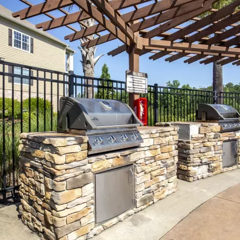 Close-up of outdoor grilling station with stone base and stainless steel appliances beneath a wooden pergola at Lauren Ridge community area.