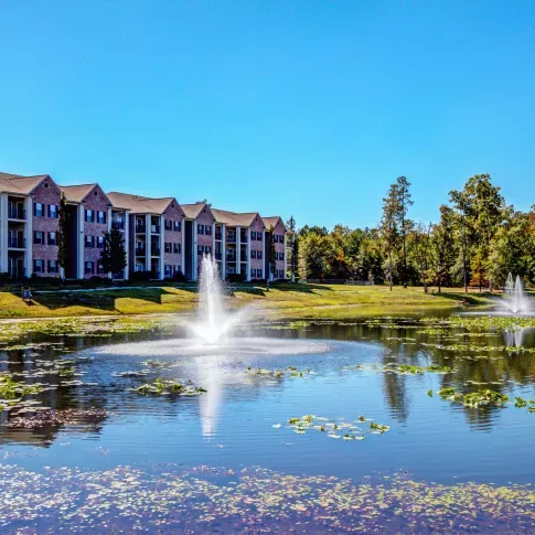 View of Lauren Ridge Apartment Homes’ brick and siding exterior with balconies, overlooking a large pond with central fountain.