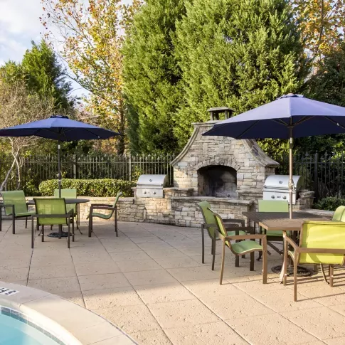 Poolside grilling station and dining area at The Heights at Lake Murray featuring stone fireplace, stainless steel grills, and umbrella-covered seating