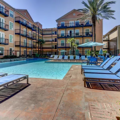 Outdoor pool area with plenty of seating and palm trees, surrounded by colorful apartment buildings at The Saulet Apartments.