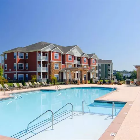 Resort-style outdoor swimming pool at Knob Creek Apartments surrounded by lounge chairs and vibrant apartment buildings.