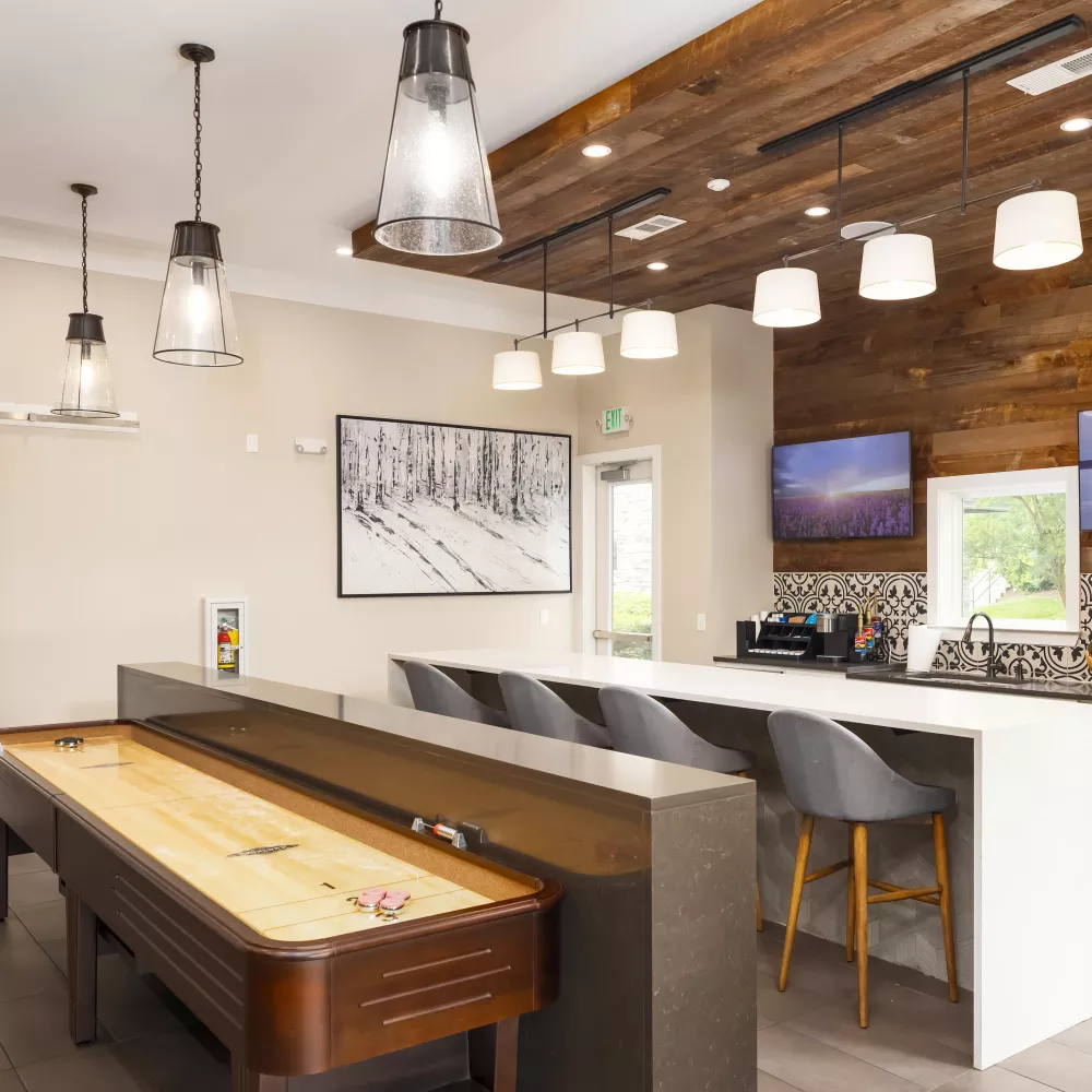 Resident game lounge at Avery Turkey Creek with shuffleboard table, bar seating, and pendant lighting.