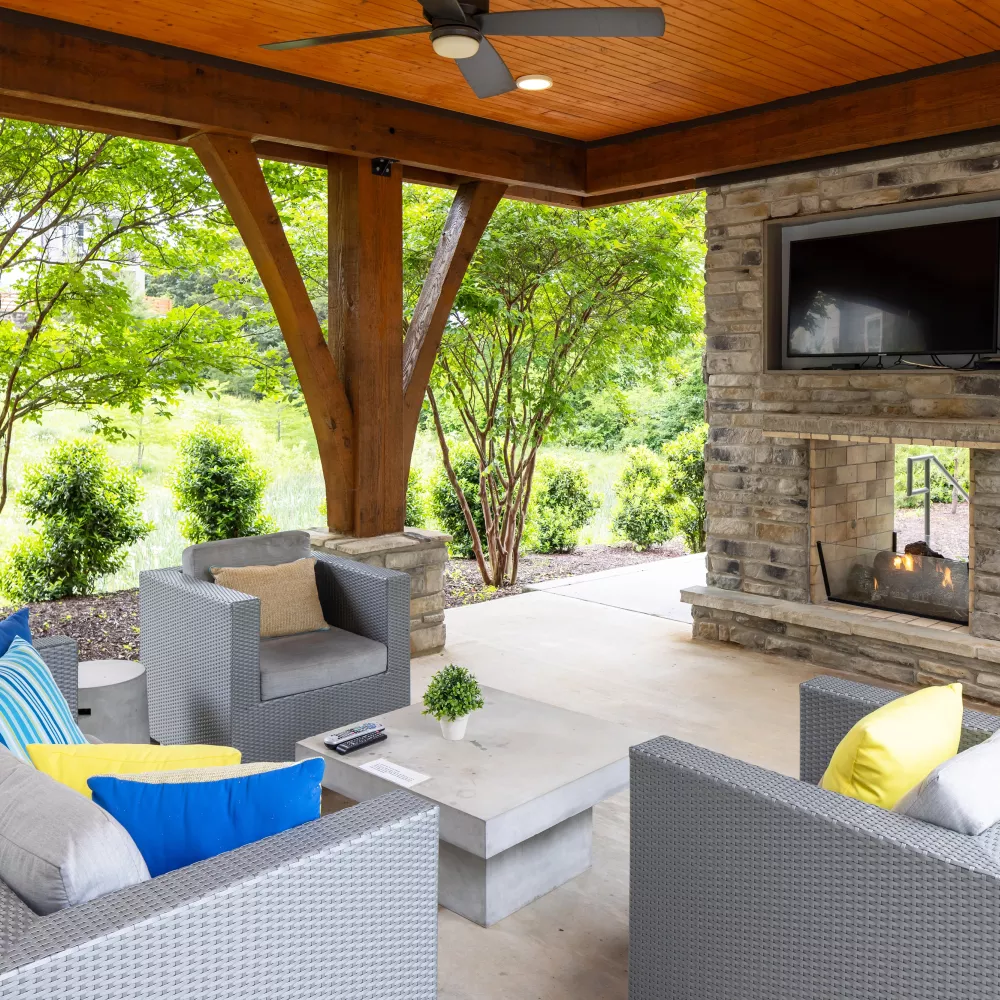 Outdoor lounge with stone fireplace, TV, and modern wicker seating at Avery apartments.