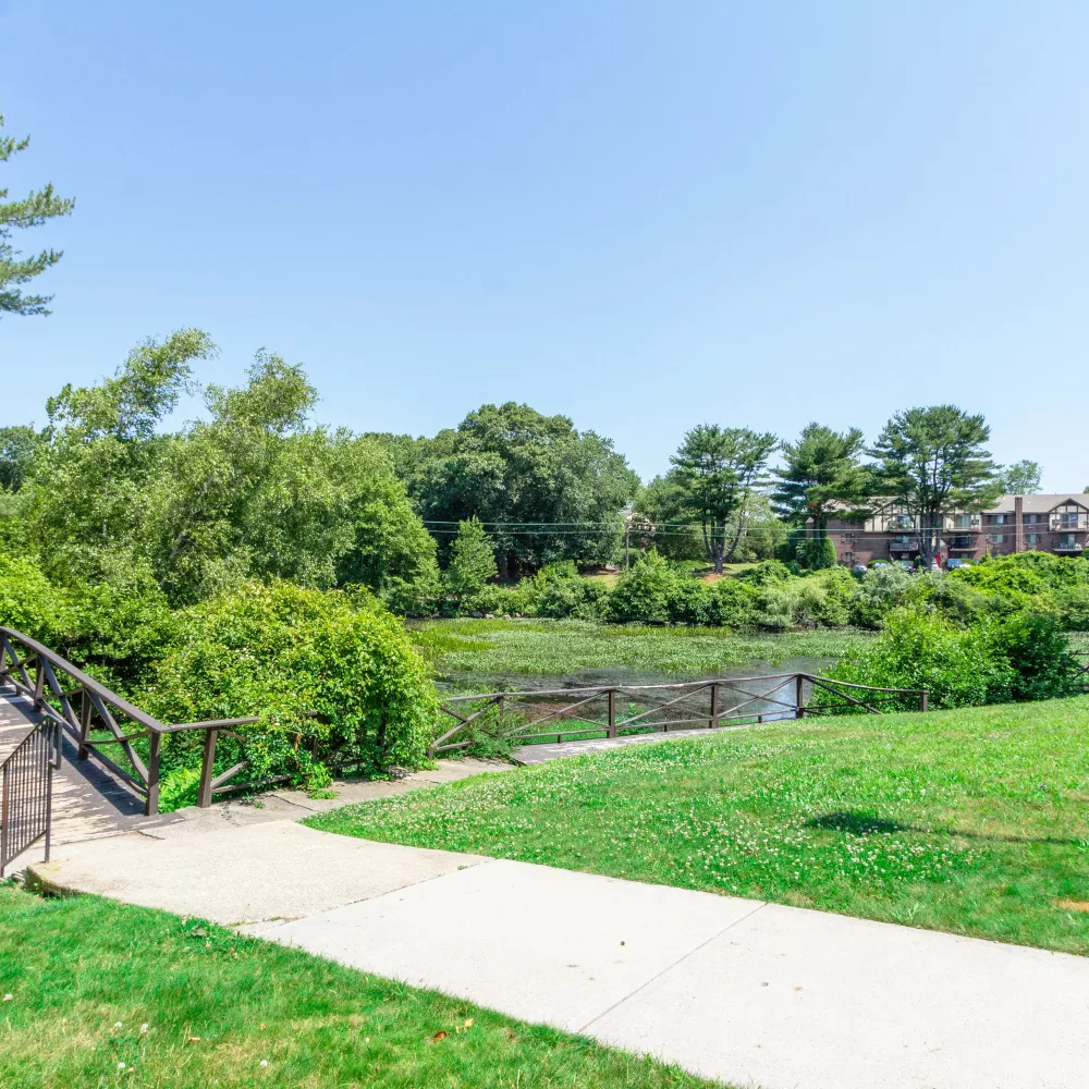 Footbridge and walking path overlooking wooded pond and greenery at Royal Crest Estates Warwick in Warwick, RI.