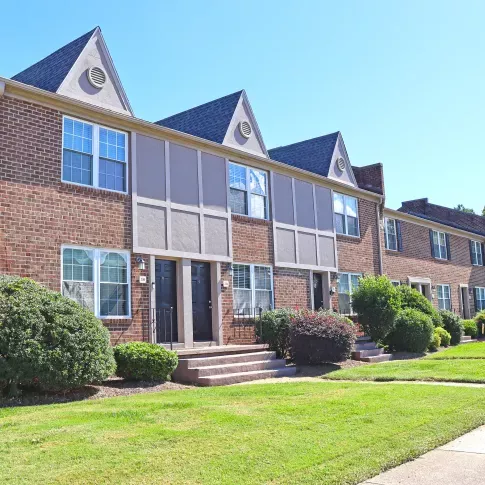 Exterior view of Maple Bay Apartments featuring well-maintained landscaping, walking paths, and a resident with a dog, showcasing the pet-friendly community atmosphere.
