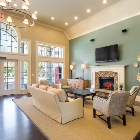 Brightly lit clubhouse lounge with comfortable seating, fireplace and large windows overlooking the pool area.